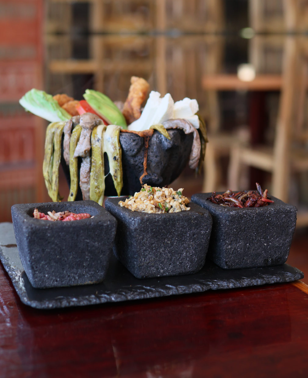 Molcajete de carne con nopales y aguacate, servido con escamoles, chinicuiles y chapulines en morteros de piedra volcánica